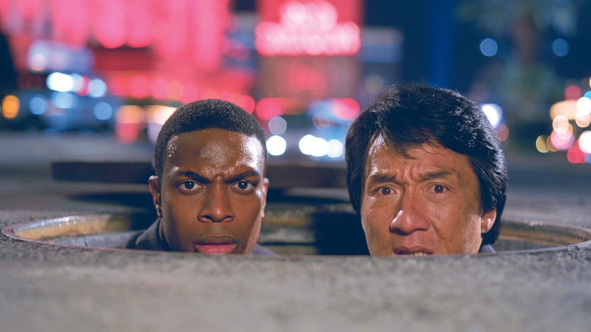 Jackie Chan and Chris Tucker emerging from a manhole on a neon-lit Hong Kong street in Rush Hour 2